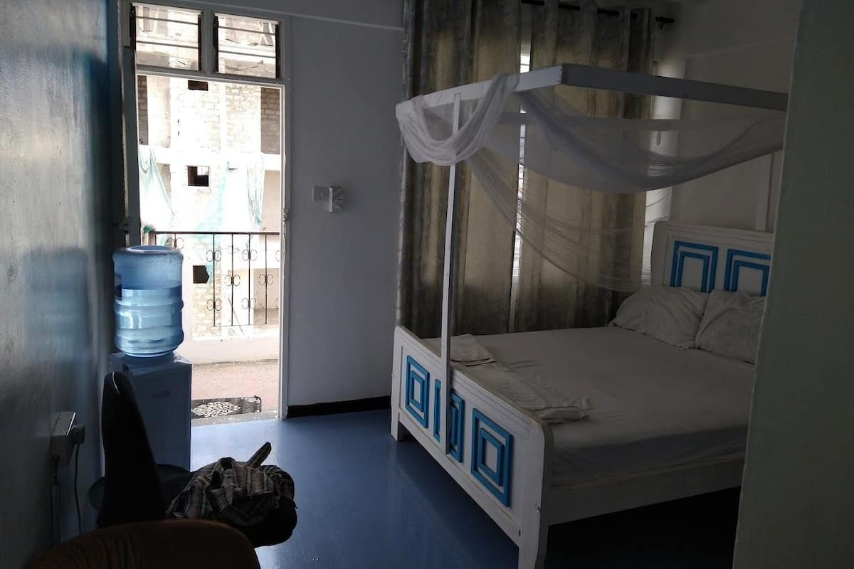A room with a bed, a water dispenser, and a view of the outside.