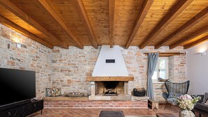 Una sala de estar acogedora con vigas de madera a la vista, chimenea de piedra, televisor de pantalla plana y asientos cómodos.