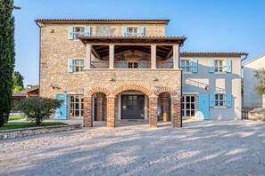A two-story stone building with a balcony, arched entrance, and blue shutters. - Historic Istrian Villa: Private Pool, Breakfast & Hot Tub (Višnjan)