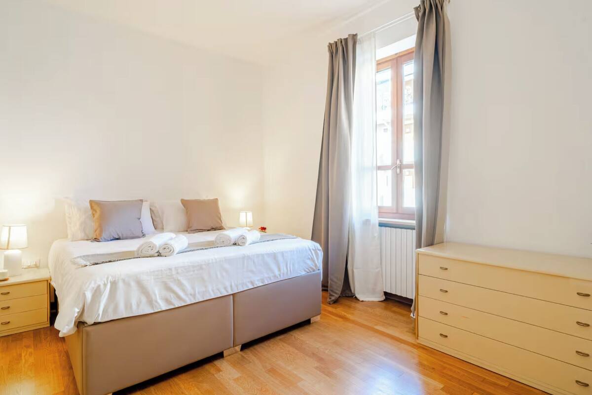 A bedroom with a bed, bedside tables, a dresser, and a window with curtains.