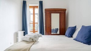 A neatly made bed with white linens and rolled towels, a wooden wardrobe, and blue curtains. - Terrazze Di Cesy (Brescia)