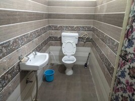 A bathroom with a toilet, sink, and blue bucket.