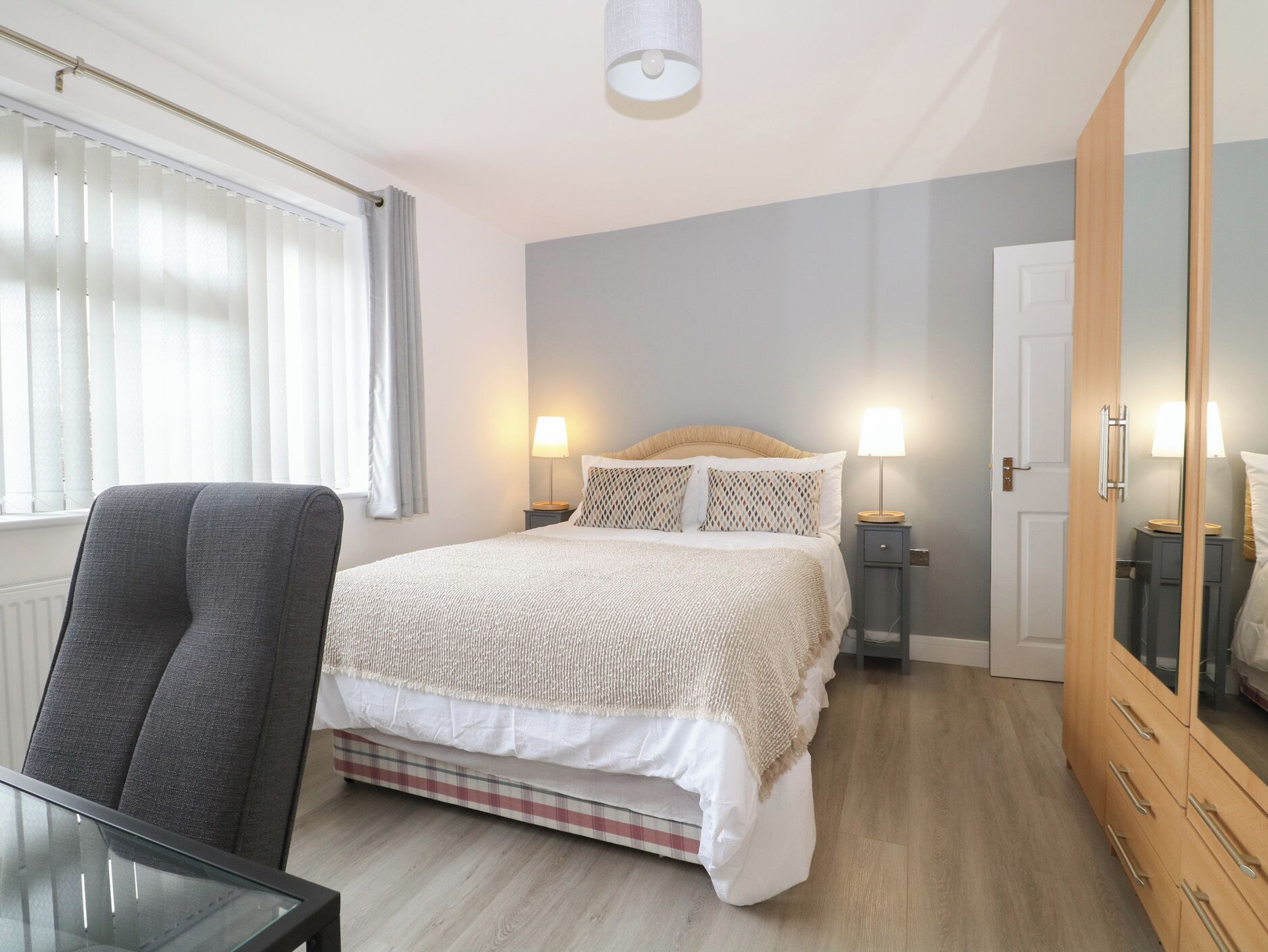 A bedroom with a bed, a chair, a desk, a wardrobe, and a window with curtains.