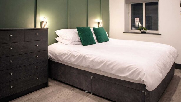 Un dormitorio moderno con cama, cómoda, lámparas de noche y ventana.