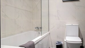 Un baño moderno con ducha de vidrio, bañera blanca y retrete.