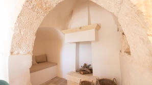Una habitación acogedora con un arco de piedra, un banco, una chimenea y dos cestas de mimbre.