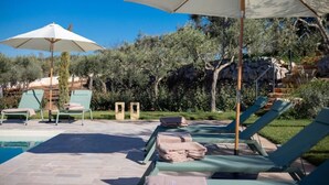 Un área junto a la piscina con sillones reclinables, sombrillas y una vista despejada del paisaje circundante.