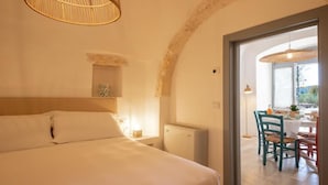 Un dormitorio con una cama grande, una mesita de noche con una lámpara, y vistas a un comedor con sillas y una mesa.