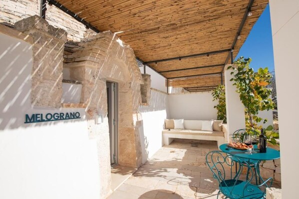 A covered outdoor area with a stone wall, a bench, and a table with chairs. - Borgo Cucumo (Castellana Grotte)