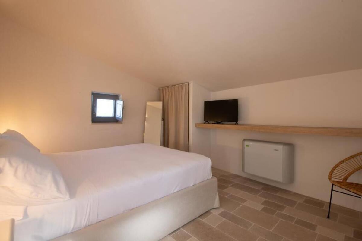 A bedroom with a bed, a TV on a shelf, a radiator, and a chair.