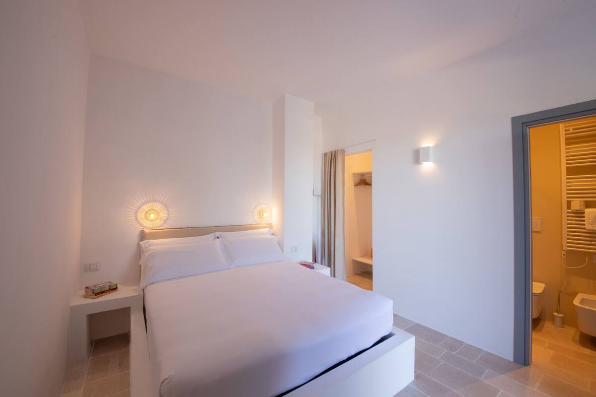 A modern bedroom with a bed, bedside tables, and a bathroom visible through an open door.