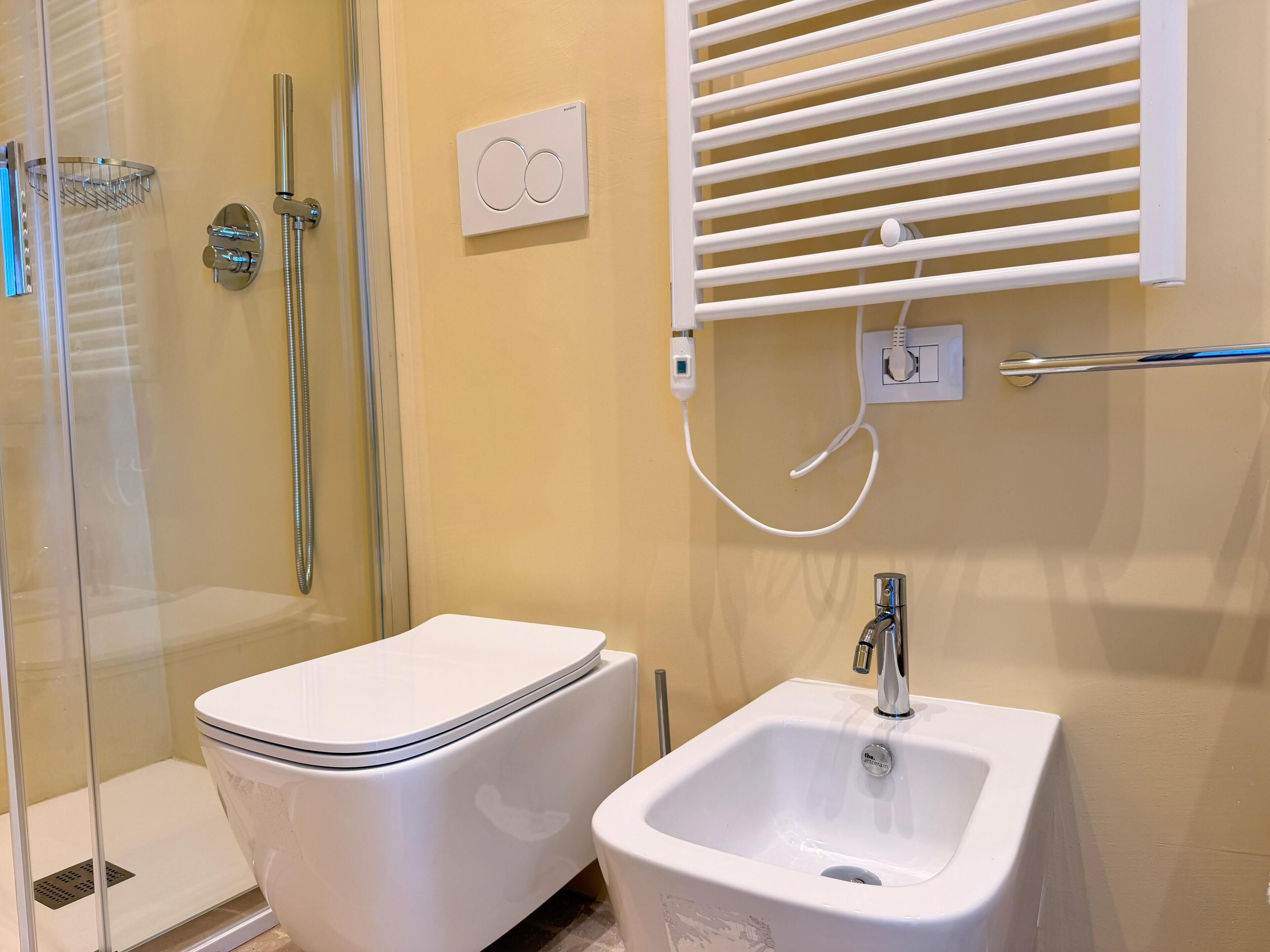 Ein Badezimmer mit Dusche, Toilette, Waschbecken und einem an der Wand angebrachten Thermostat.