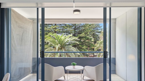 A balcony with a view of trees, two chairs, a small table, and a potted plant. - MetaWiseBnB |Cronulla Beach Walk to Train & Shops1 (Cronulla)