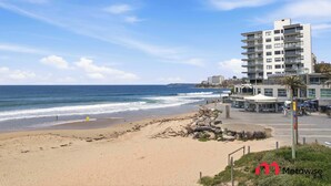 A beach with a building that has multiple balconies and a restaurant area. - MetaWiseBnB |Cronulla Beach Walk to Train & Shops1 (Cronulla)