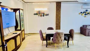 Un coin repas avec une table et des chaises, un téléviseur posé sur un meuble, et un élément décoratif mural.