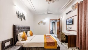 Une chambre d’hôtel comprenant un lit, une table de chevet, un bureau avec une chaise, une télévision et une fenêtre avec des rideaux.