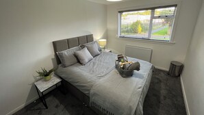 Ein Schlafzimmer mit Bett, Nachttisch, Lampe, Fenster und Heizkörper.