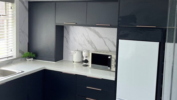 Eine moderne Küche mit dunklen Schränken, einer weißen Arbeitsplatte, einer eingebauten Mikrowelle und einem Kühlschrank.