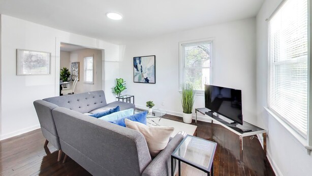 Un soggiorno moderno con un divano grigio, una TV a schermo piatto e un'area pranzo con tavolo e sedie.
