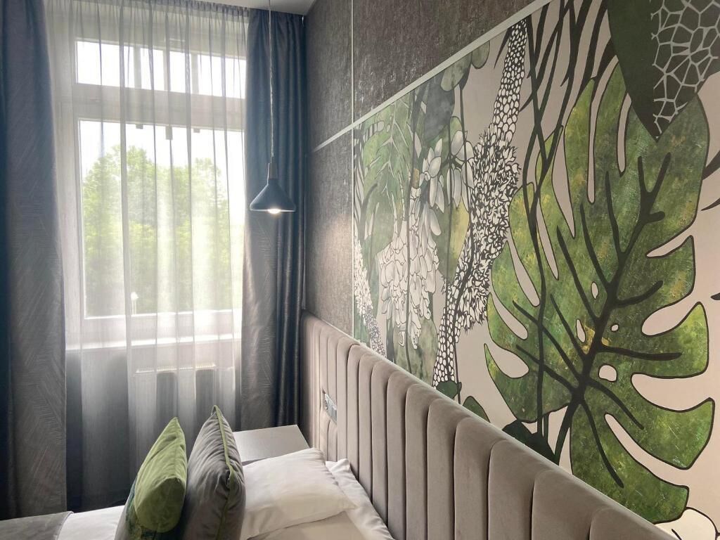 A bedroom with a bed, a window with curtains, and a wall mural of leaves.