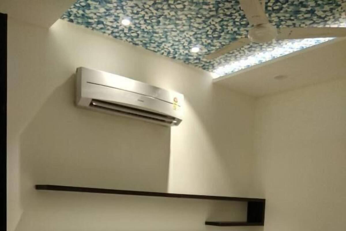 Une chambre d’hôtel comprenant un lit, une table de chevet, un appareil de climatisation et un plafond orné d’un motif bleu et blanc.