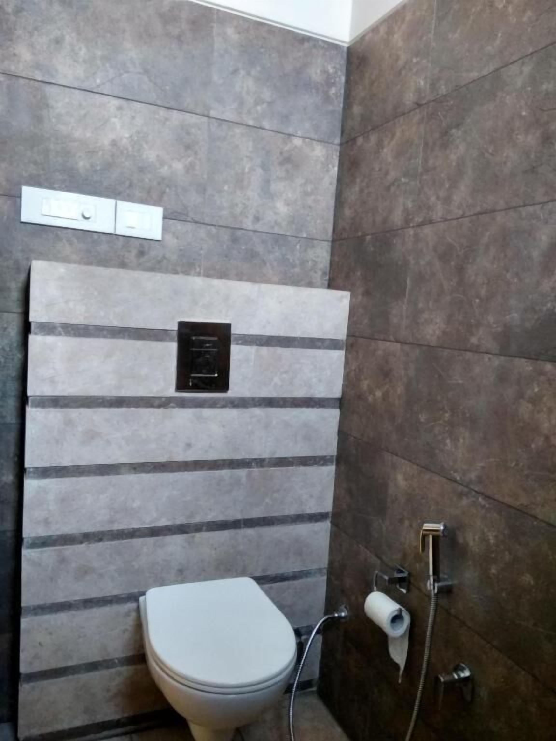 A bathroom with a toilet, a towel dispenser, and a toilet paper holder.