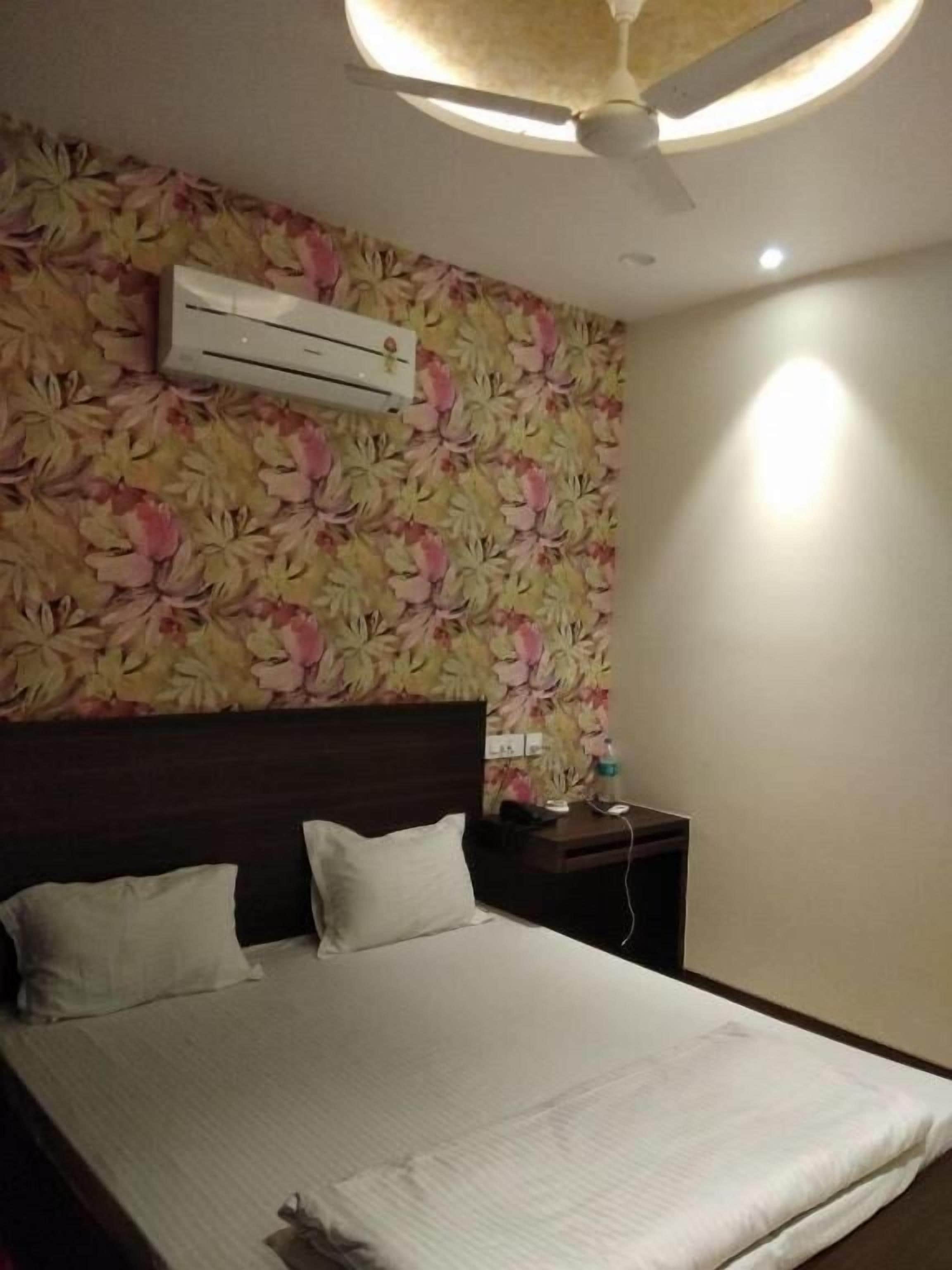 A hotel room with a bed, a nightstand, a wall-mounted air conditioner, and a ceiling fan.
