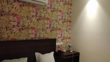 A hotel room with a bed, a nightstand, a wall-mounted air conditioner, and a ceiling fan.