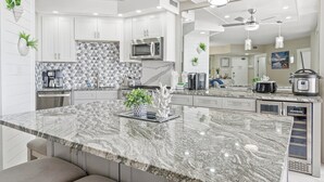A modern kitchen with white cabinetry, a granite countertop, and a central island with a plant. - Gulf-Front Luxury | Surfside 11th Floor | #1109 | 2B/2Ba (Miramar Beach)