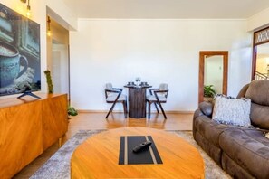 Ein modernes Wohnzimmer mit einem Holztisch, einem braunen Ledersofa und einem Essbereich mit zwei Stühlen und einem kleinen Tisch.