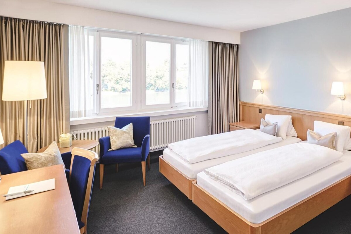 A hotel room with two beds, a desk, a chair, and a window with curtains.