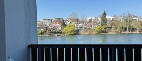 Un balcon avec vue sur une rivière, des bâtiments et des arbres.