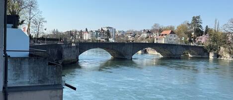Un río con un puente de piedra, edificios al fondo y un cielo despejado.