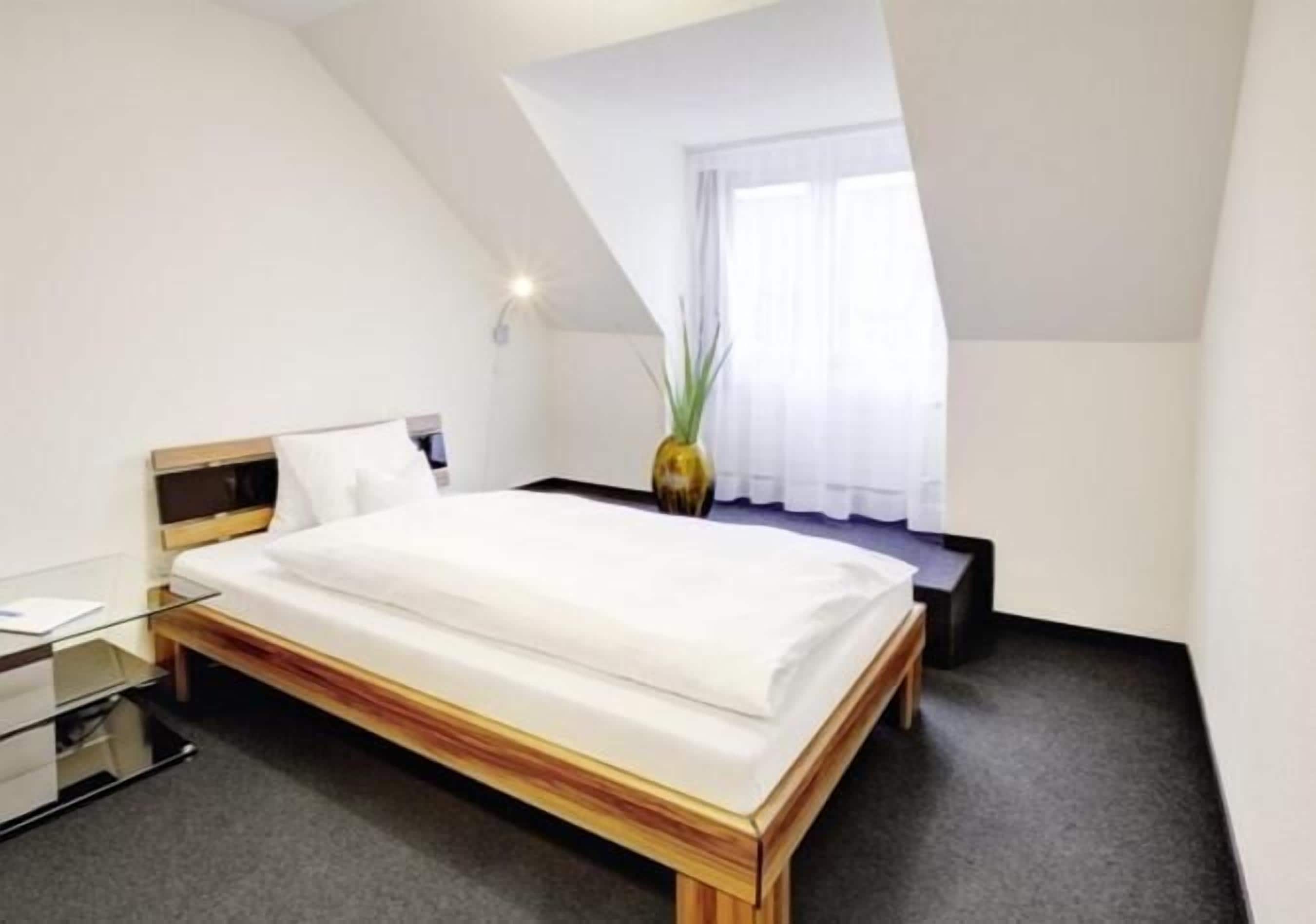 Camera d'albergo moderna con un letto in legno, una scrivania in vetro e un piccolo tavolino.