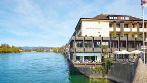 Ein Hotel mit Blick auf den Fluss, Außenplätzen und einer Flagge.