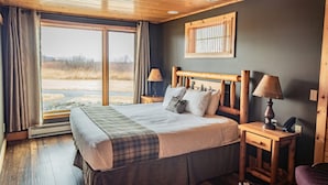 Une chambre à coucher avec un grand lit, une tête de lit en bois, deux tables de chevet avec des lampes, une fenêtre avec des rideaux et une vue sur l’extérieur.