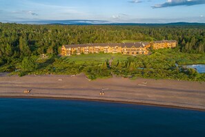 Un gran edificio de estilo cabaña con varios pisos, rodeado de un bosque denso y una playa.