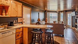 A kitchen with wooden cabinets, a central island with stools, a sink, and a dining area with a table and chairs. - Northwoods At The Lodge Two Bedroom Suite (Two Harbors)