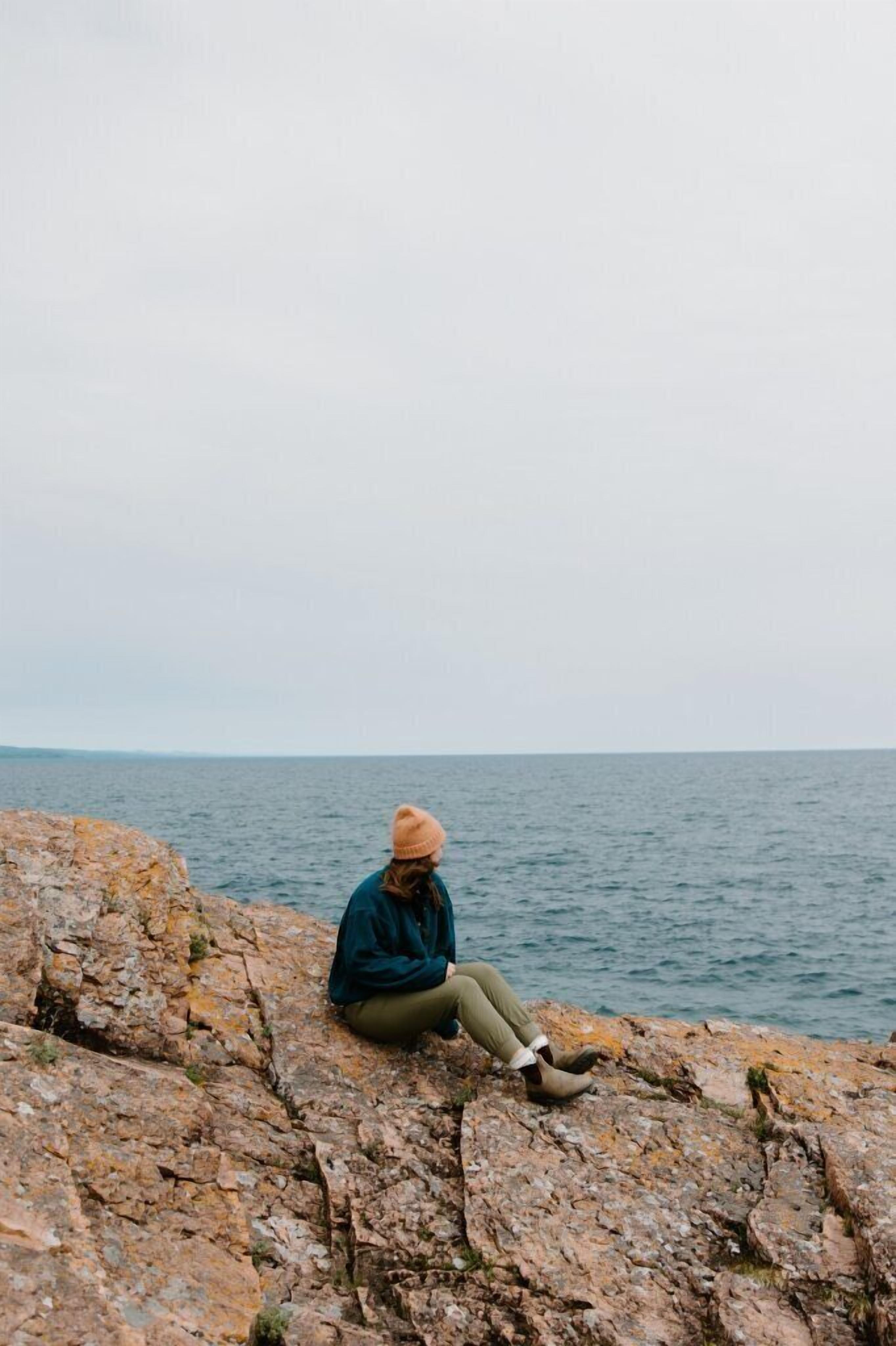 A person sitting on a rocky surface by the sea.