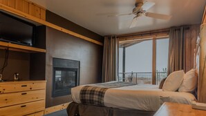 Un dormitorio con cama, televisión, chimenea, muebles de madera y balcón con vistas.