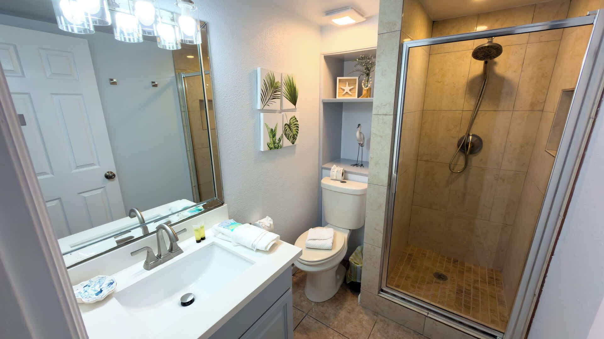 Une salle de bain moderne avec une douche à parois de verre, un lavabo blanc avec un miroir et des toilettes.
