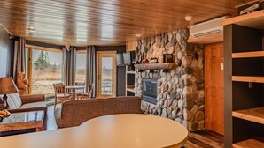 Una sala de estar acogedora con chimenea de piedra, techo de madera y un ventanal con vistas al exterior.