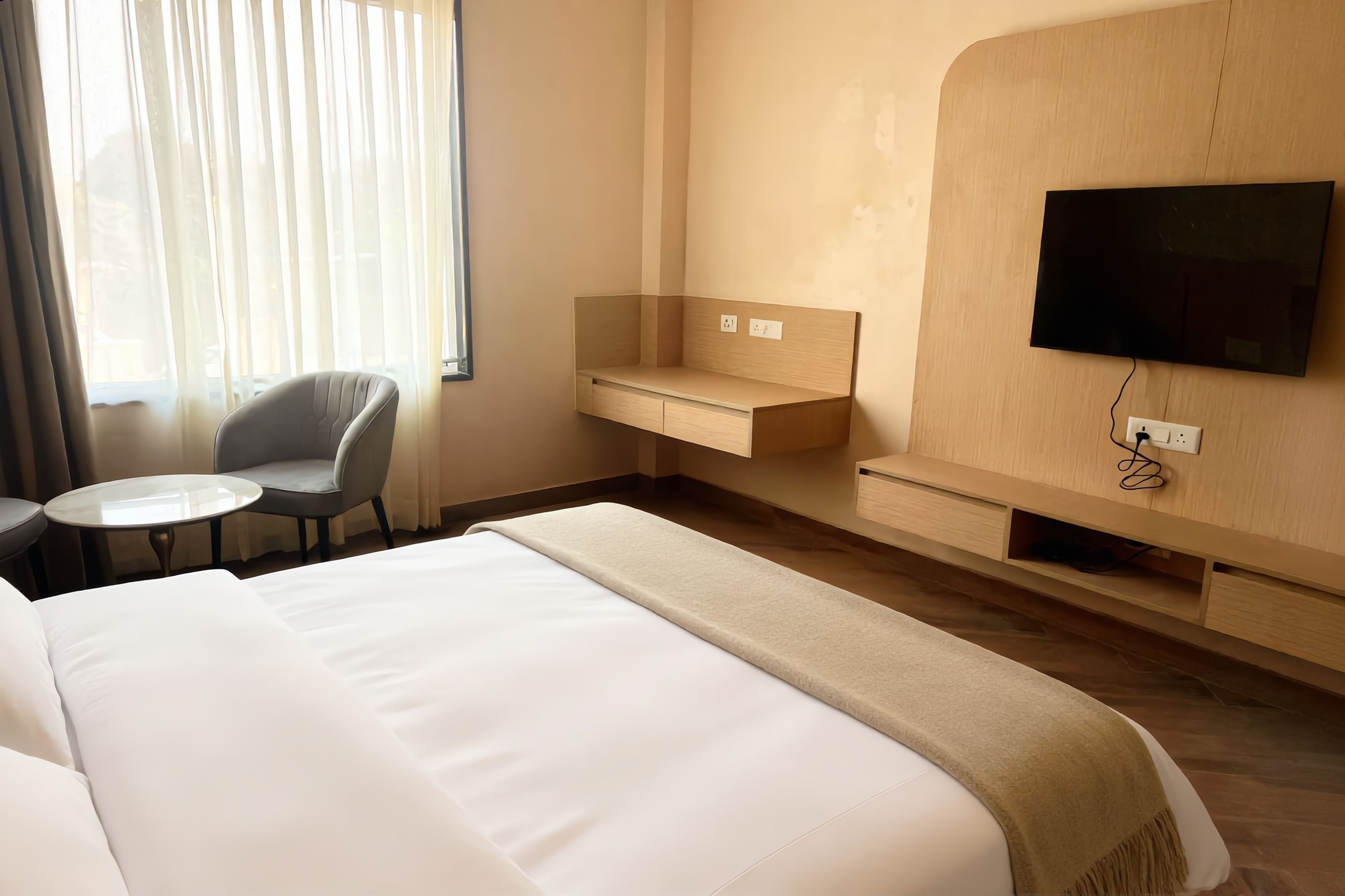 Ein Hotelzimmer mit einem großen Bett, einem Schreibtisch, einem Sessel, einem an der Wand befestigten Fernseher und einem fenster mit Vorhängen.