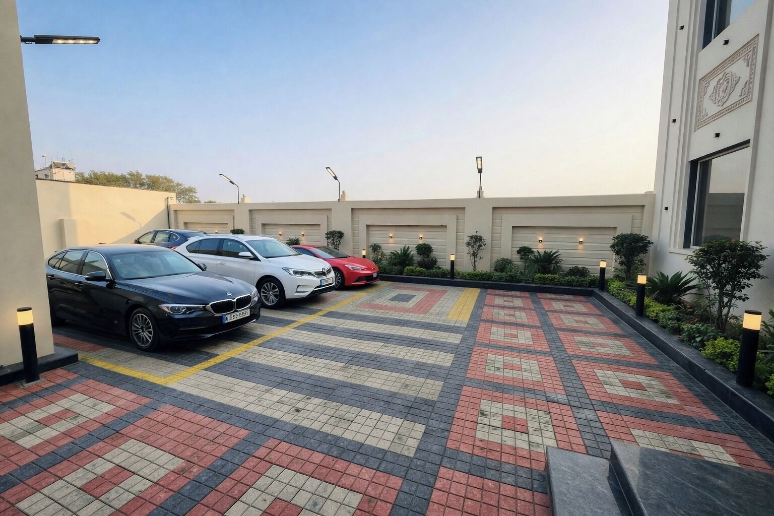A parking area with three cars, a patterned tile floor, and a building with garage doors.
