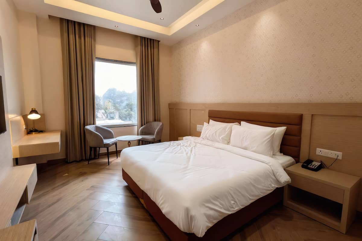 Ein Hotelzimmer mit einem großen Bett, einem Schreibtisch, einem Stuhl, einem kleinen Tisch und einem Fenster mit Vorhängen.