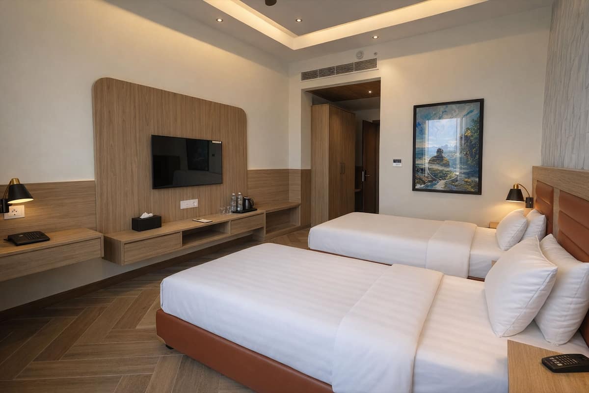 Ein Hotelzimmer mit zwei Betten, einem an der Wand befestigten Fernseher, einem Gemälde und einem hölzernen Kopfteil.