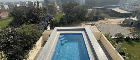 A rectangular swimming pool with a tiled edge, surrounded by a low wall and a garden area with various plants.