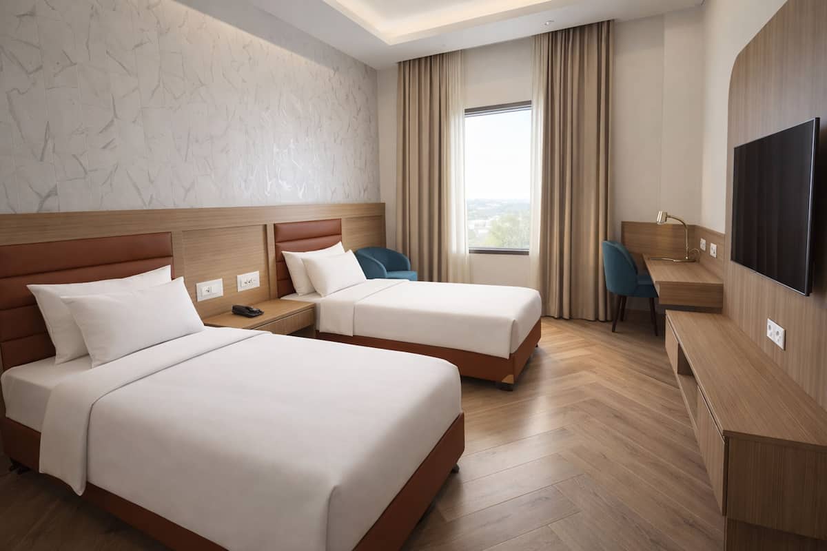 Ein Hotelzimmer mit zwei Betten, einem Schreibtisch, einem Stuhl, einem Fernseher und einem Fenster mit Vorhängen.