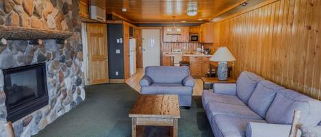 Un intérieur de chalet chaleureux avec une cheminée en pierre, des murs en bois, un coin cuisine et des sièges confortables.