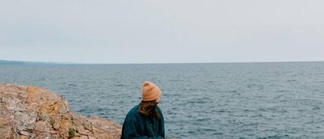 Una persona asseguda sobre una roca a la vora del mar.